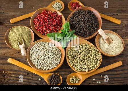 Various colorful peppercorns in the bowls and spoons on wooden table. Stock Photo