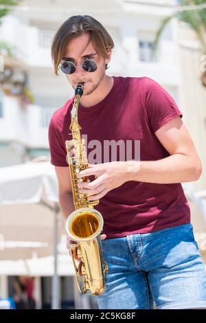 Handsome young man playing a saxophone while looking at the camera on an out of focus background. Music and lifestyle concept. Stock Photo
