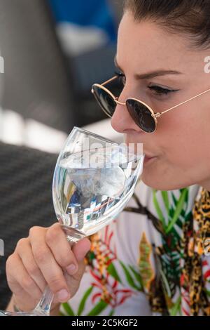 Close up of a beautiful woman wearing glasses drinking from a glass of water with ice cubes on it on an out of focus background. Healthy lifestyle and Stock Photo