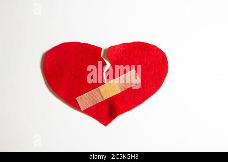 Broken heart and glued together with a band-aid. A heart from felt. A concept about broken love. Heart with plaster isolated on white background Stock Photo