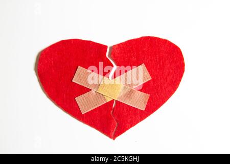 Broken heart and glued together with a band-aid. A heart from felt. A concept about broken love. Heart with plaster isolated on white background Stock Photo