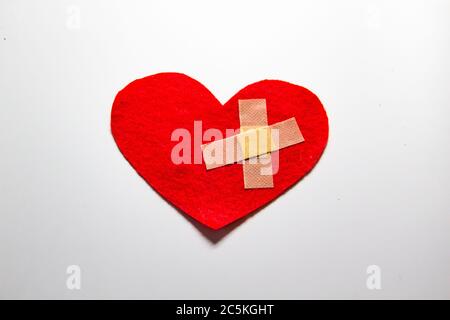 Broken heart and glued together with a band-aid. A heart from felt. A concept about broken love. Heart with plaster isolated on white background Stock Photo