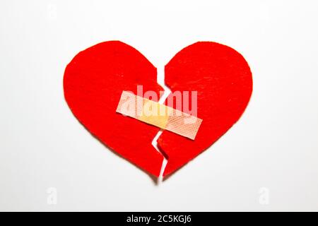 Broken heart and glued together with a band-aid. A heart from felt. A concept about broken love. Heart with plaster isolated on white background Stock Photo