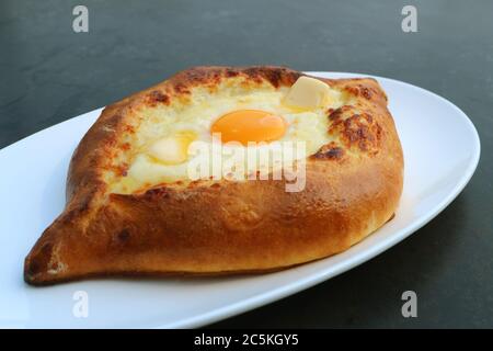 Adjarian Khachapuri, a Plate of Traditional Georgian Bread Filled with Cheese and Fresh Egg on Black Table Stock Photo