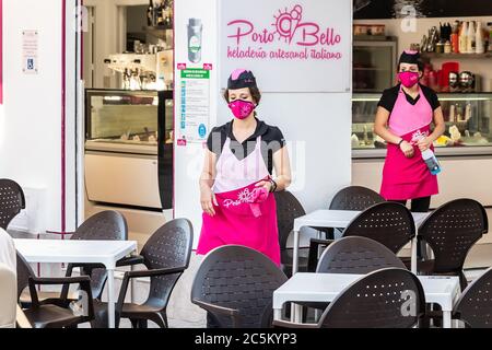 Punta Umbria, Huelva, Spain - June 3, 2020: A woman waitress  in a protective mask is going to clean the tables of Porto Bello ice cream parlour in th Stock Photo