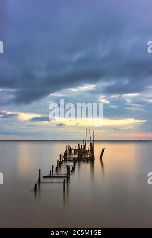 Morning scenery with rain clouds in the sky and golden light from the sun at a fishing village with an old, broken wooden bridge. Stock Photo