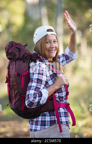 Portrait active attractive mature woman hiking happy and relaxed with backpack in the woods, waving with one hand, blurred background Australian wilde Stock Photo