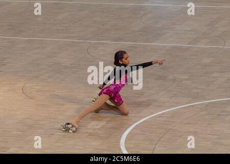 Little girl on roller skates of figure skating in a competition with black and pink dress Stock Photo