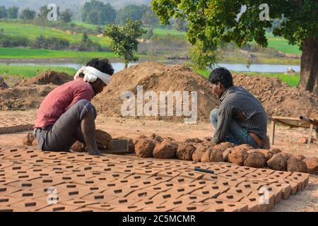 TIKAMGARH, MADHYA PRADESH, INDIA - FEBRUARY 07, 2020: Unidentified happy Indian men making house bricks by hand using a mold and wet clay. Stock Photo