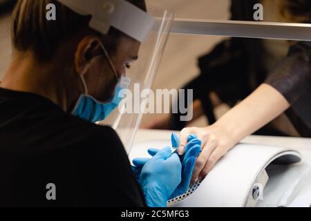 Aesthetician doing the manicure, filing the nails with a file to his client in a beauty center Stock Photo