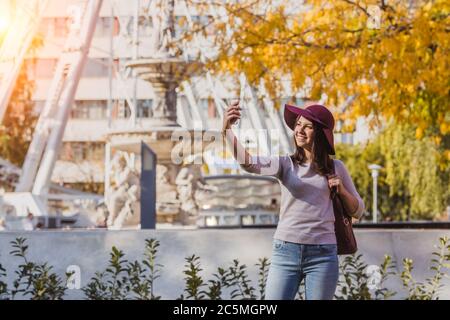A happy young woman take selfie photo near the Budapest Eye big Ferris wheel in Budapest Stock Photo