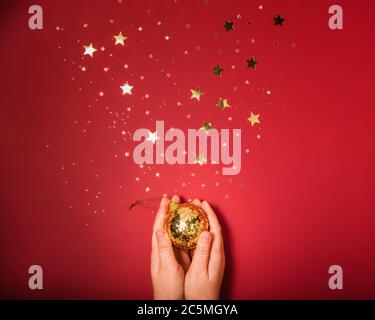 Female hands holding the golden ball on red background with gold stars sparkles Stock Photo