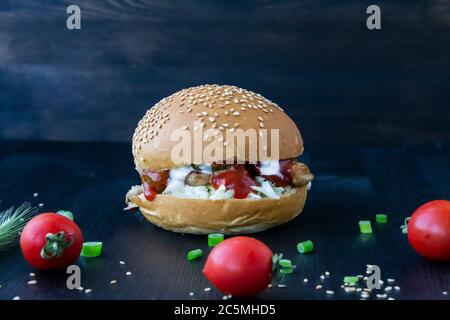 Tasty burger with fried pork slices, cabbage in sauce, canned cucumbers and ketchup on the wood background Stock Photo