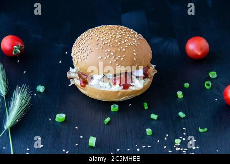 Tasty burger with fried pork slices, cabbage in sauce, canned cucumbers and ketchup on the wood background Stock Photo
