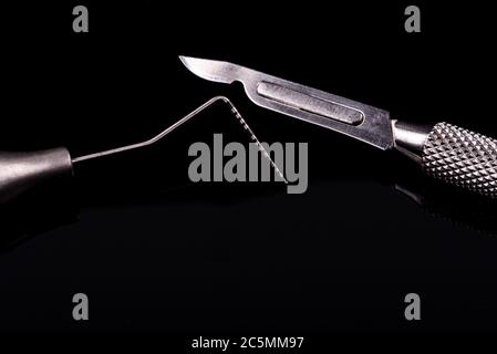 Horizontal color image with a front view of a professional dental tools on a black background. Periodontal probe and scalpel. Stock Photo