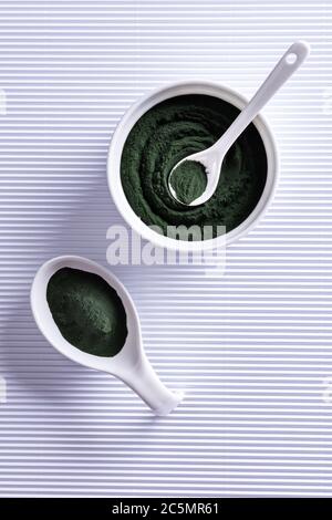 Green chlorella or spirulina powder in white porcelain bowl, large spoon and in small spoon. Healthy superfood eating and dieting concept. Stylish whi Stock Photo