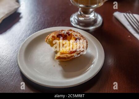 A Portuguese custard tart on a plate in a coffee shop, with a bite taken out of it Stock Photo