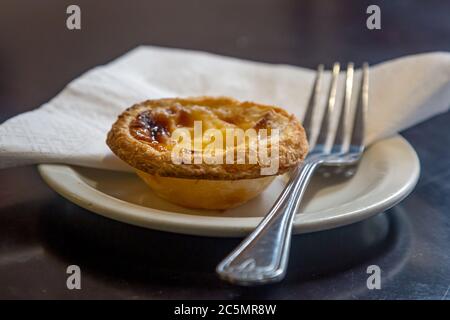 A Portuguese custard tart on a plate in a coffee shop, ready to be eaten Stock Photo