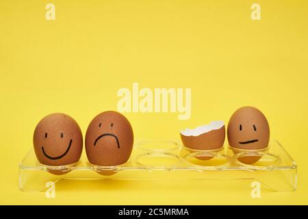 Chicken eggs in an egg holder. Full tray of eggs. Half an egg, egg yolk, shell. Emotion and facial expression painted on eggs. Stock Photo