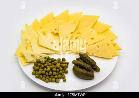 Beautiful plate with sliced ​​cheese, cucumbers and green peas isolated on a white background. Keto diet with very healthy and tasty meal for lunch Stock Photo
