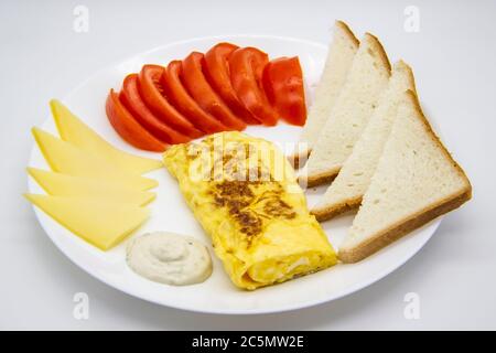 Amazing breakfast with tasty omelet, tomatoes, cheese, bread and sauce on the white plate. Delicious omelet made like rolle, other ingredients. Tasty Stock Photo