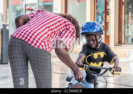 Punta Umbria, Huelva, Spain - June 3, 2020: The mother is helping her son to ride in bike in the street Calle Ancha in Punta Umbria, Spain Stock Photo