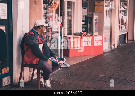 A big issue seller on the the street sitting alone waiting to sell copies Stock Photo