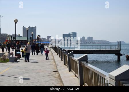 Vladivostok, Russia - April 28, 2019: People walking along of sea on promenade, city skyline on background Stock Photo