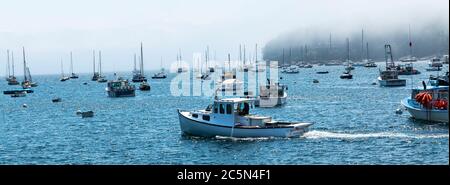 Rockport, Maine, USA - 4 August 2017: A fishing boat moving through many moored sailboats and loster boats on a foggy morning in Bar Harbor Maine. Stock Photo