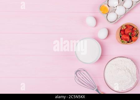 Flat lay composition of ingredients for baking homemade strawberry pie, eggs, flour, sugar and fresh berries on a pink background. Stock Photo