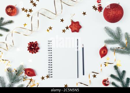Blank notebook among red Christmas decorations, golden confetti and green fir branches on white background, flat lay. Stock Photo