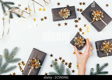 Christmas flat lay composition female hand holds gift box next to golden ribbons, spruce branches and confetti on white background with an empty place Stock Photo