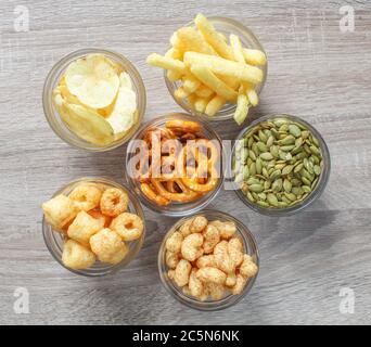 Top view of different types of snacks on wooden table. Crisps and treats from above. Stock Photo