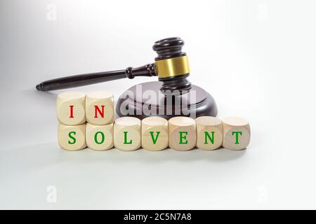 Wooden dices with the word Insolvent and a judge gavel, some companies have to give up during the coronavirus crisis, gray background with copy space, Stock Photo