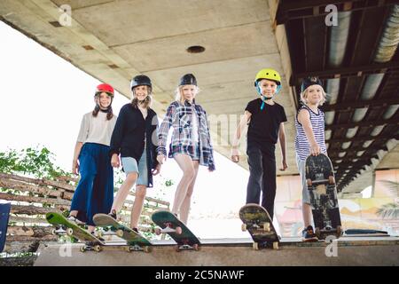 Group of friends children at skate ramp. Portrait of confident early teenage friends hanging out at outdoor city skate park. Little skateboarders Stock Photo