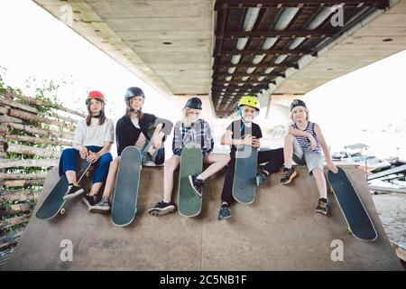 Group of friends children at skate ramp. Portrait of confident early teenage friends hanging out at outdoor city skate park. Little skateboarders Stock Photo
