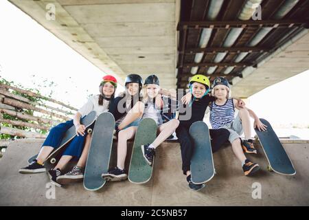 Group of friends children at skate ramp. Portrait of confident early teenage friends hanging out at outdoor city skate park. Little skateboarders Stock Photo