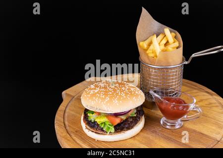 Fresh tasty burger and fried potatoes with red sauce on a wooden board isolated on black Stock Photo