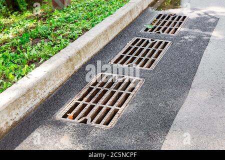 hatch storm system with a rusty grate in the asphalt road surface with a stone curb. Stock Photo