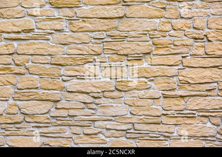 texture of the stone wall of the facade of the building decorated with tiles in layers of yellow natural stone. Stock Photo