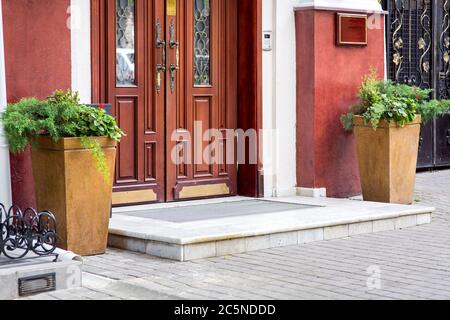 marble threshold of the entrance to the building with a wooden door and stone vases with green plants, an intercom at the front door. Stock Photo