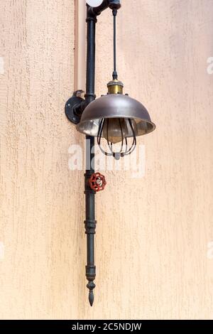 street loft lamp of black pipe and red valve on the plaster wall of the facade of the building, close up decorative lantern. Stock Photo