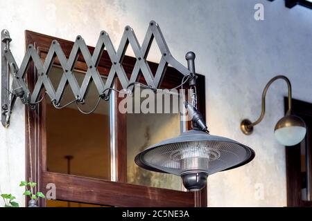 friction pantograph pendant electric heater mounted on the wall of the building facade with a brown window, black heater in the loft style close-up. Stock Photo