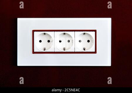 socket with plugs for standard type F plug in white plastic case on a burgundy glossy stone wall. Stock Photo