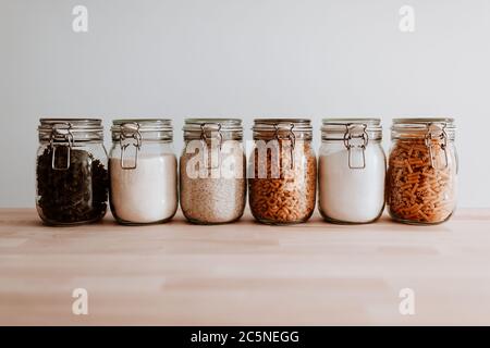 Six glass jars full with dried uncooked food ingredients on wooden table Stock Photo
