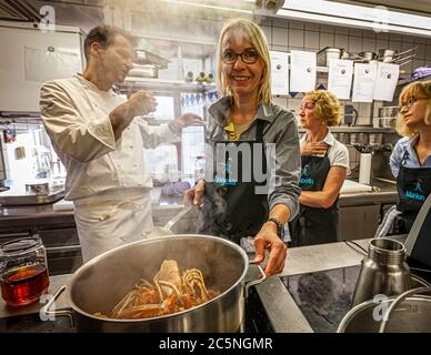 In the foreground, journalist Angela Berg stirs steaming langostinos in a large pot during a cooking class in the kitchen of Wernberg Castle, Wernberg-Köblitz, Upper Palatinate, Germany. In the background, participants Elisabeth and Marion look on alongside Michelin-starred chef Thomas Kellermann. The course traditionally concludes with the signature dish of langostinos as its fourth course. Stock Photo