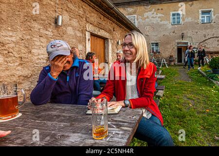 Josef, a Zoigl connoisseur from the northern Upper Palatinate, laughs with journalist Angela Berg at a wooden table of the Zoigl inn in the old rectory of Altenstadt an der Waldnaab, Upper Palatinate, Germany. Photographer Georg Berg met Josef by chance; he arrived by bicycle and knows historical as well as amusing stories about the region's Zoigl culture. Beer mugs stand on the table. Stock Photo