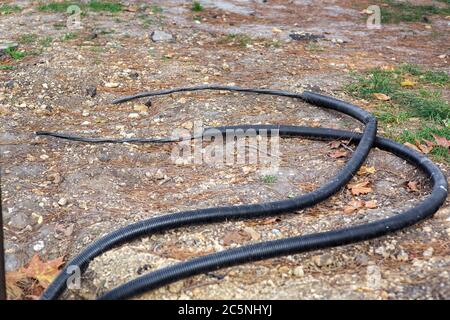 two power cables in insulation and protective corrugated jackets lie on the ground. Stock Photo