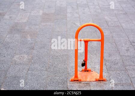 parking lock device orange color mounted on a gray square paving slabs, close-up front view. Stock Photo