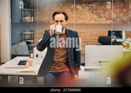 Bearded man in brown shirt and black jacket resting at work Stock Photo